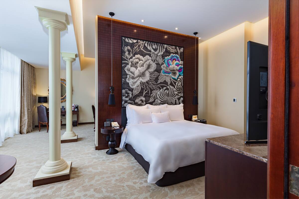 Ein Hotelzimmer mit einem großen Bett, einem Schreibtisch, einem Stuhl, einem Nachttisch und einem dekorativen Wandbild.
