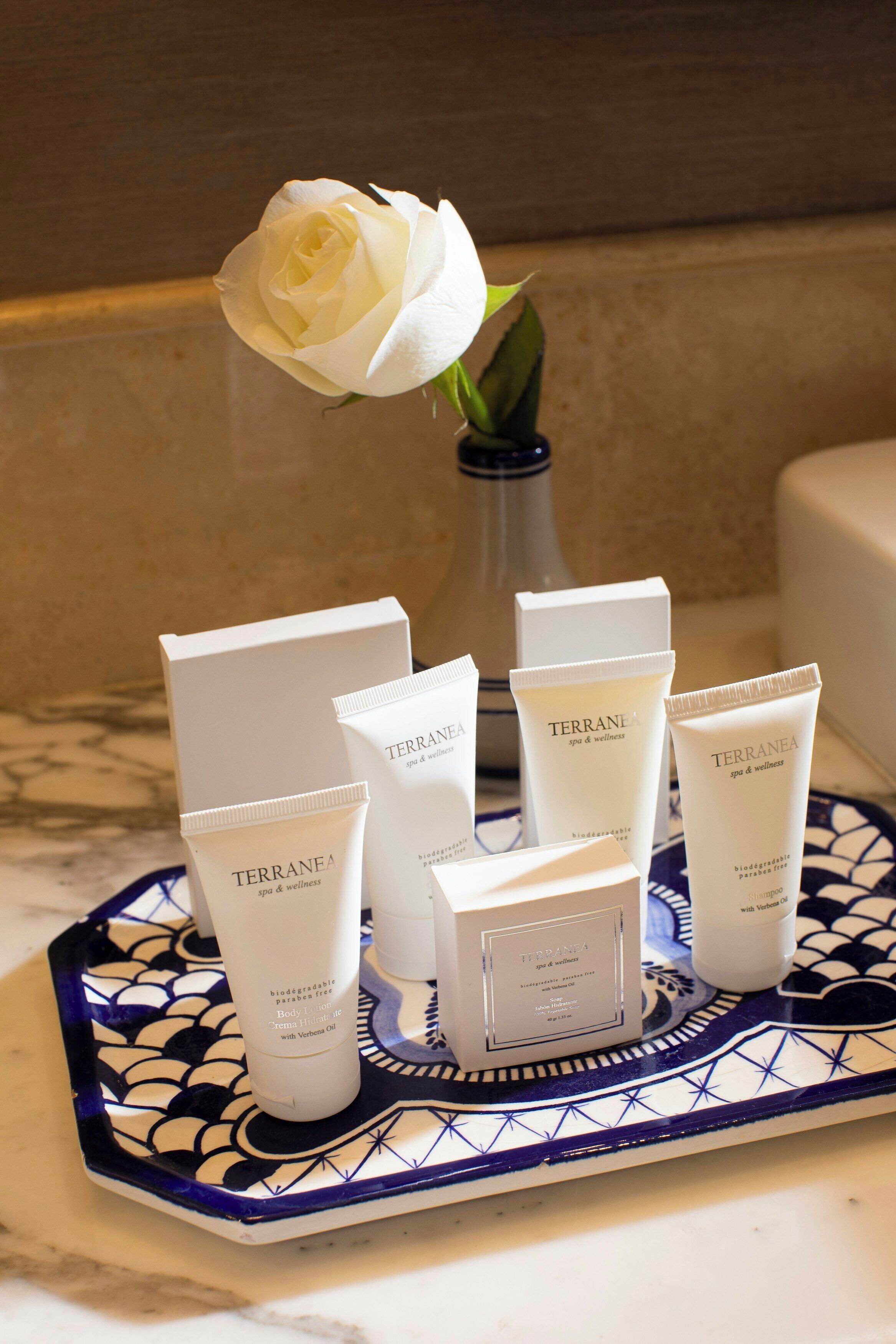 A tray with skincare products and a white rose in a vase.