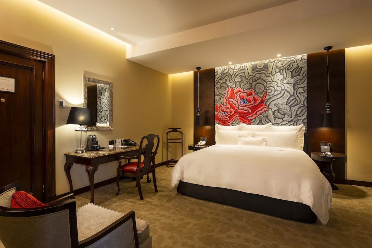 Ein Hotelzimmer mit Bett, Schreibtisch, Stuhl, Nachttischen und einer großen Blumenweberei an der Wand.