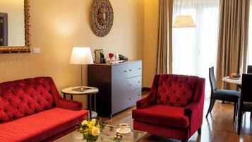 A hotel room with a red sofa, a red armchair, a small table with a vase of flowers, a lamp, and a mirror on the wall.