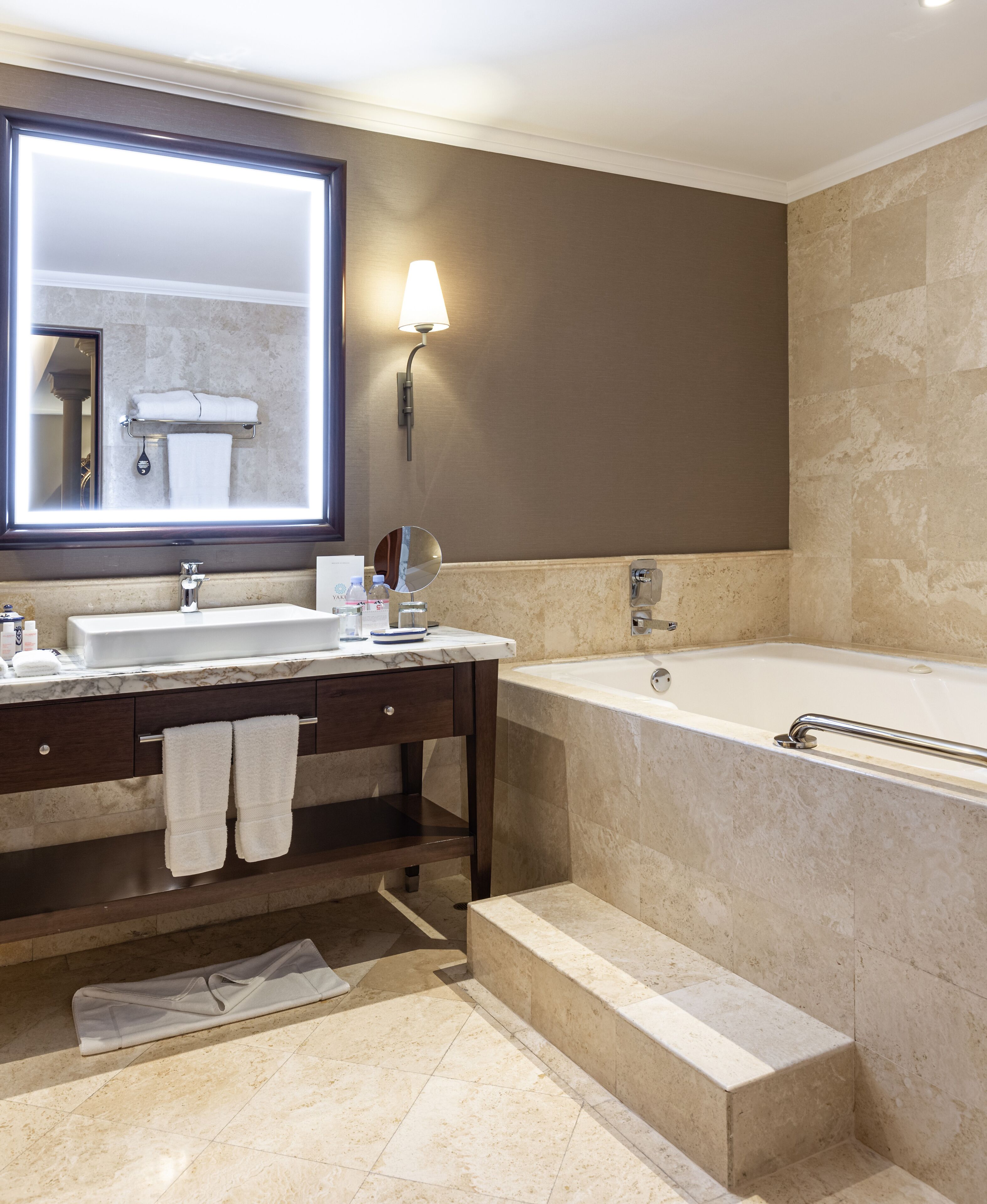 Un baño moderno con un espejo grande, dos lavamanos, una bañera y un perchero para toallas.