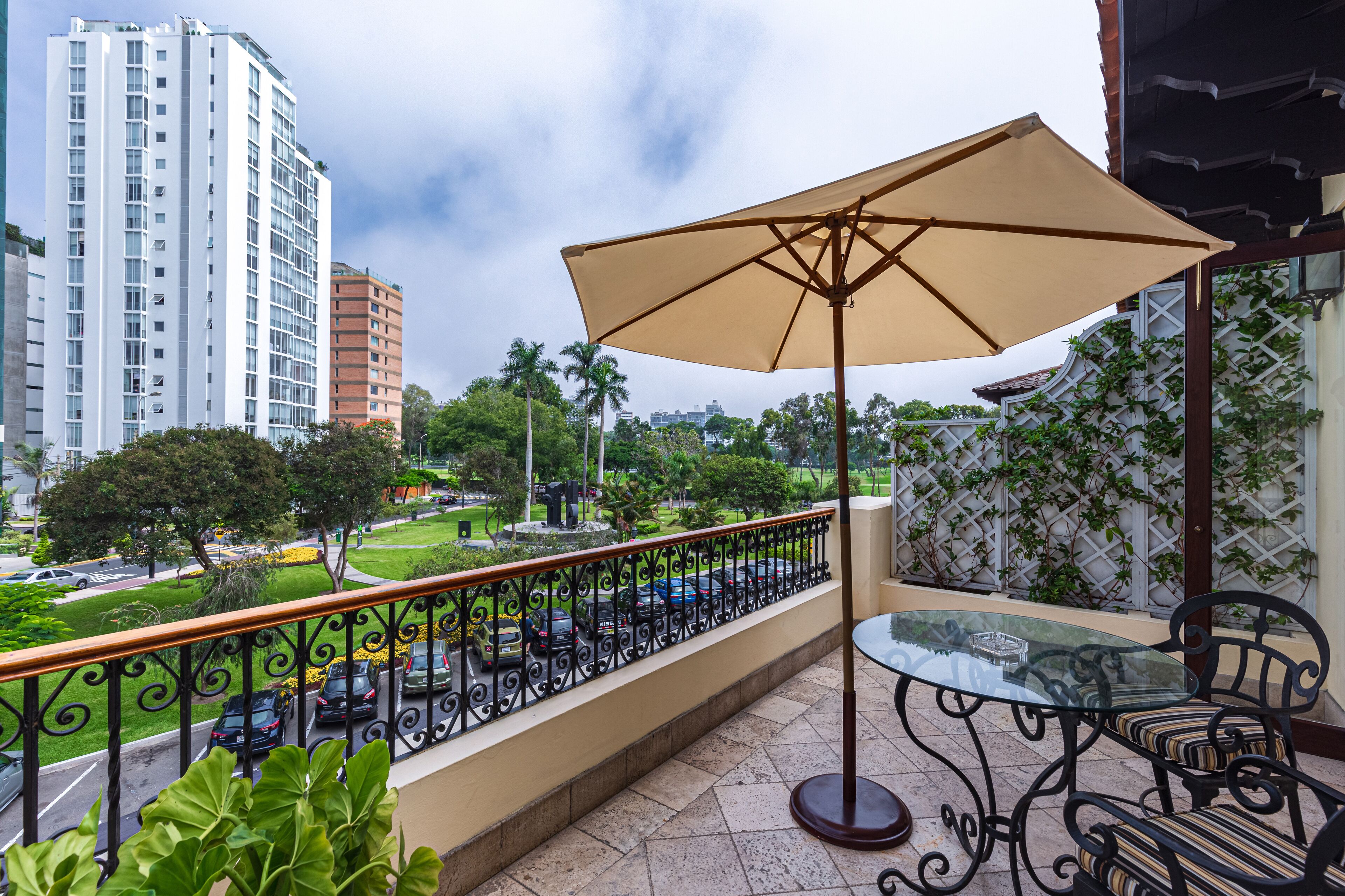 Un balcon avec une table et des chaises en verre, un parasol et une vue sur un paysage urbain avec des bâtiments et de la verdure.