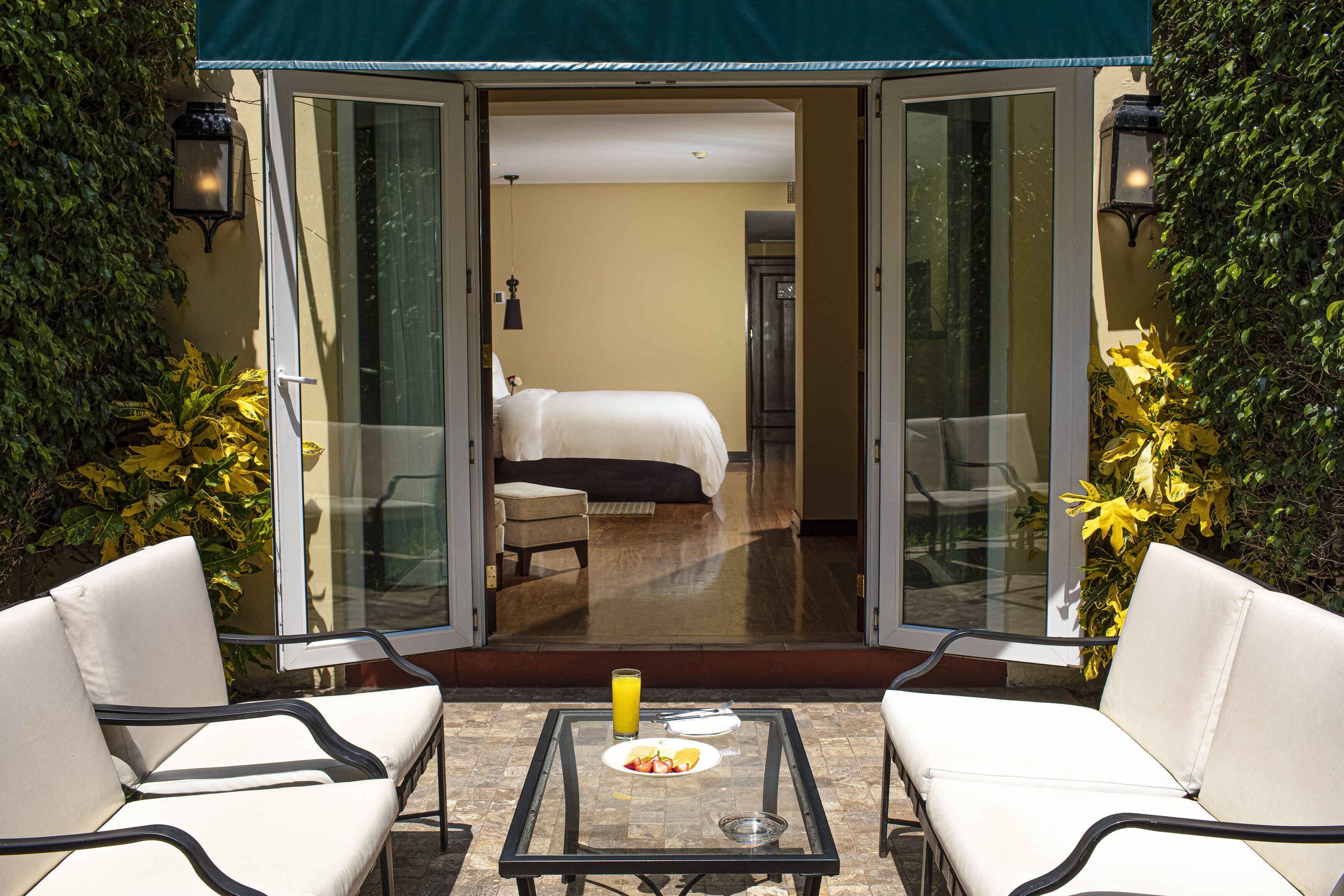 A hotel room with a glass door leading to a balcony with two white chairs and a table with breakfast items.