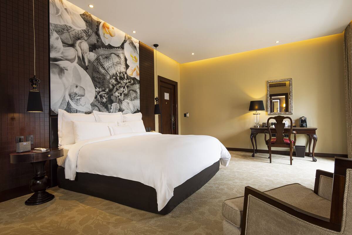 Ein Hotelzimmer mit einem großen Bett, einem Schreibtisch mit Stuhl, einem Spiegel und einer Wand mit einem großen floralen Wandbild.