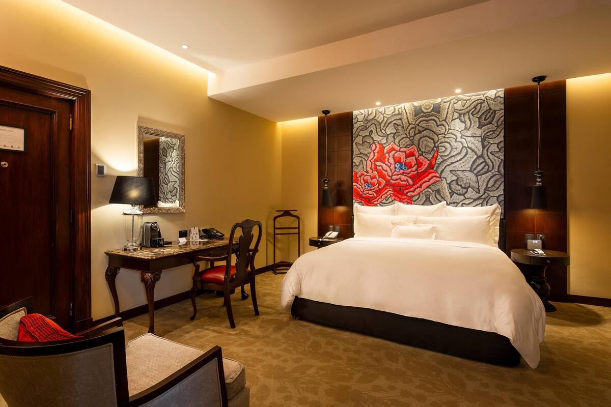 Ein Hotelzimmer mit einem großen Bett, einem Schreibtisch mit Stuhl, einer Lampe und einem Nachttisch.