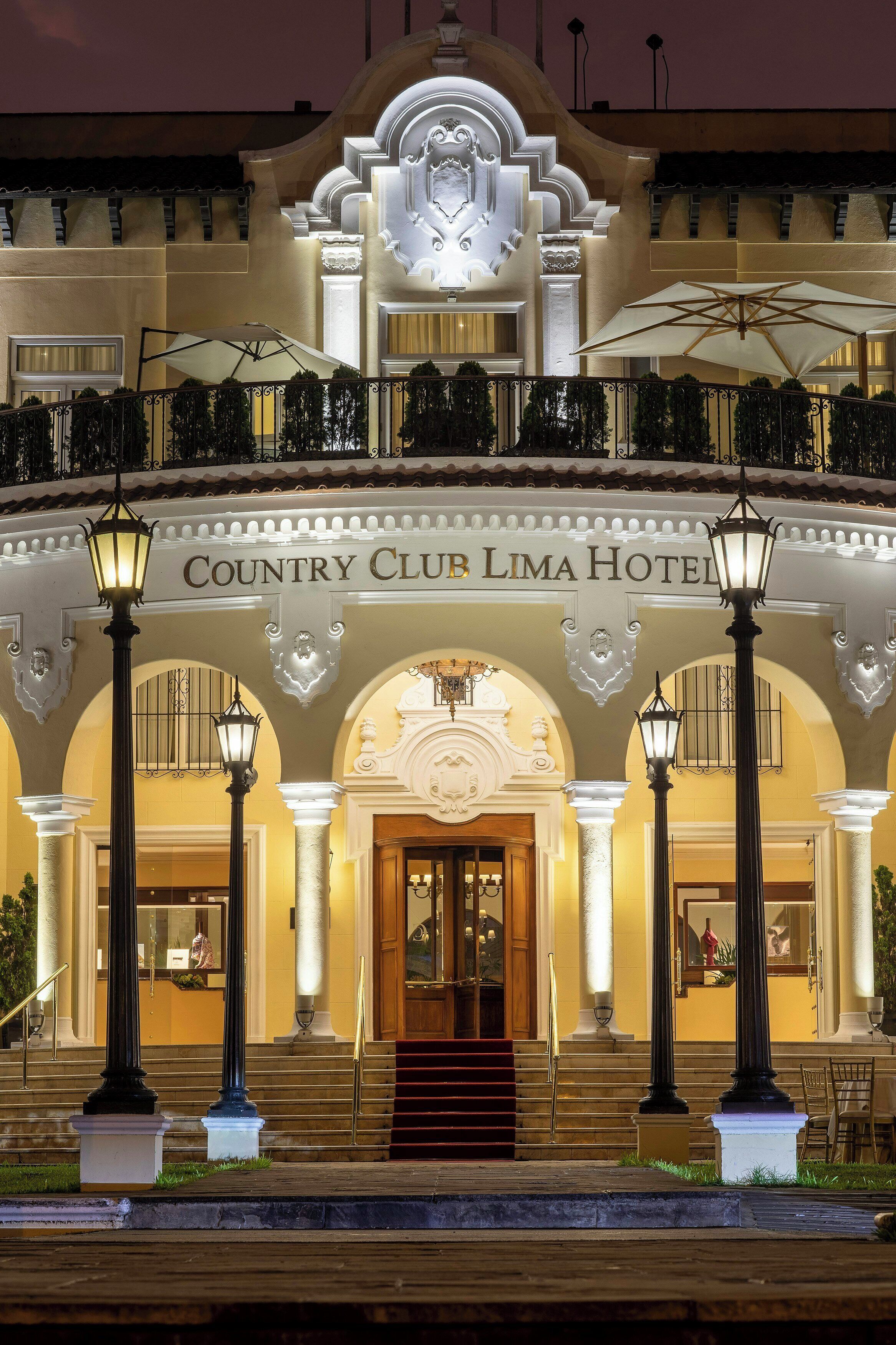 Entrada de hotel con un gran arco, escalones y zona de estar al aire libre con sombrillas.