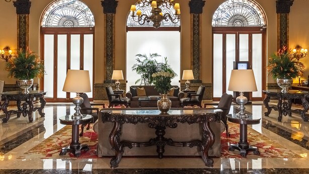 Un amplio vestíbulo con piso de mármol, muebles ornamentados y un gran candelabro.