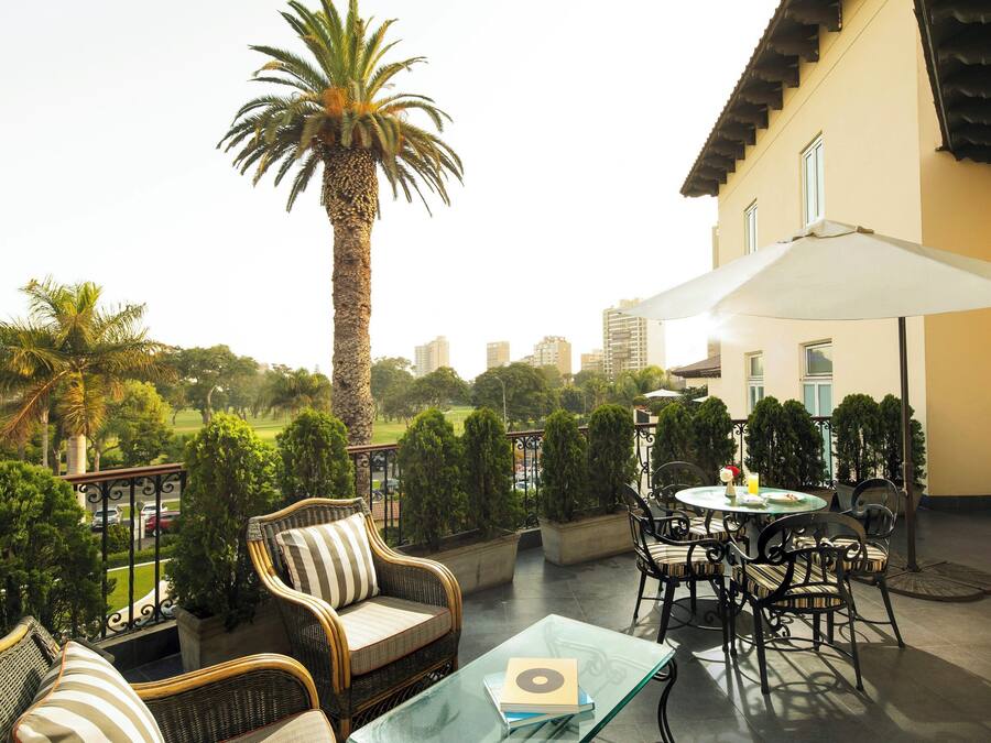 Une terrasse avec des meubles en osier, une table en verre et un palmier.