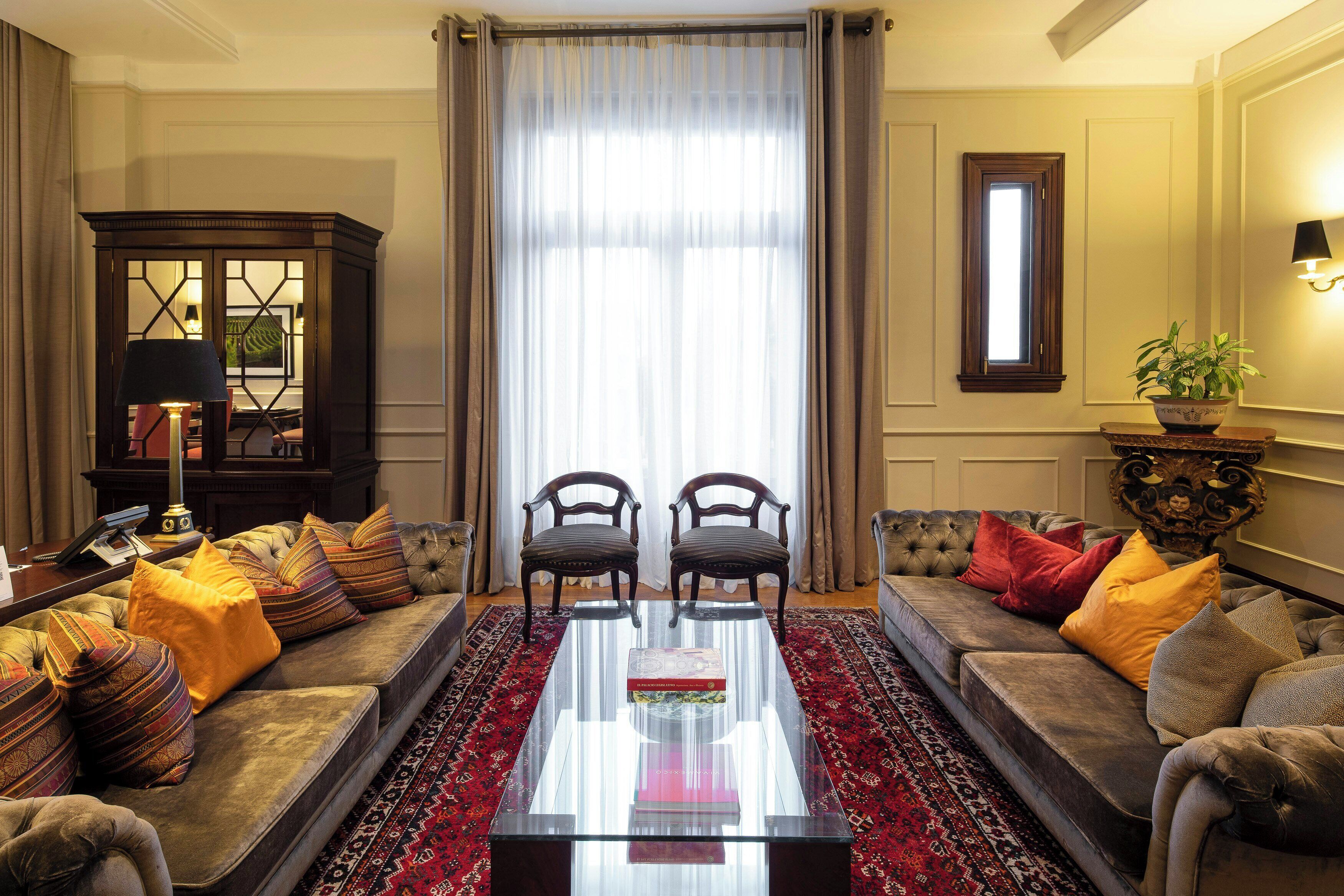 Uma sala de estar com sofá, duas poltronas, mesa de centro, aparador e uma janela grande com cortinas.