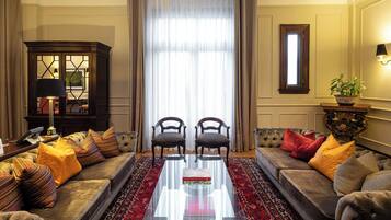 Uma sala de estar com sofá, duas poltronas, mesa de centro, aparador e uma janela grande com cortinas.