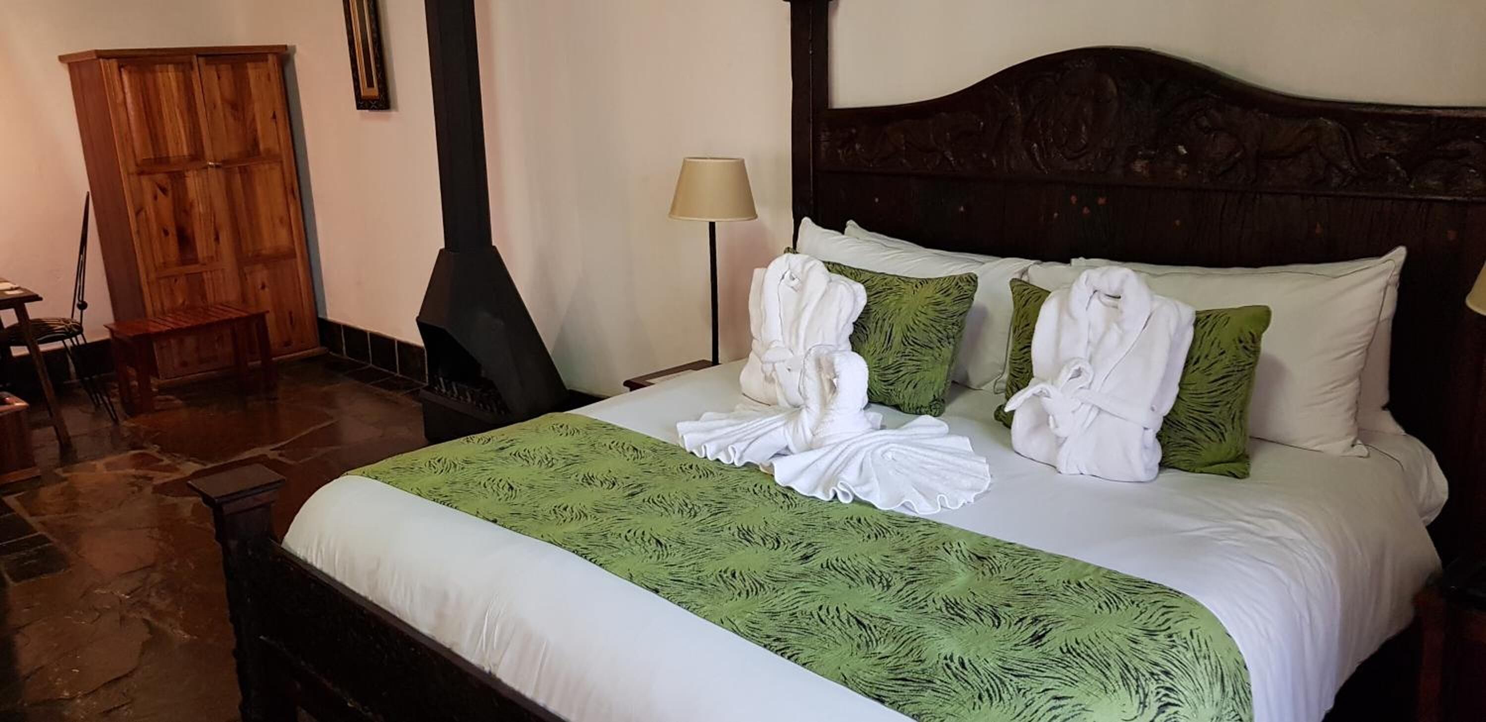 A neatly made bed with white and green linens, a wooden wardrobe, and a lamp.