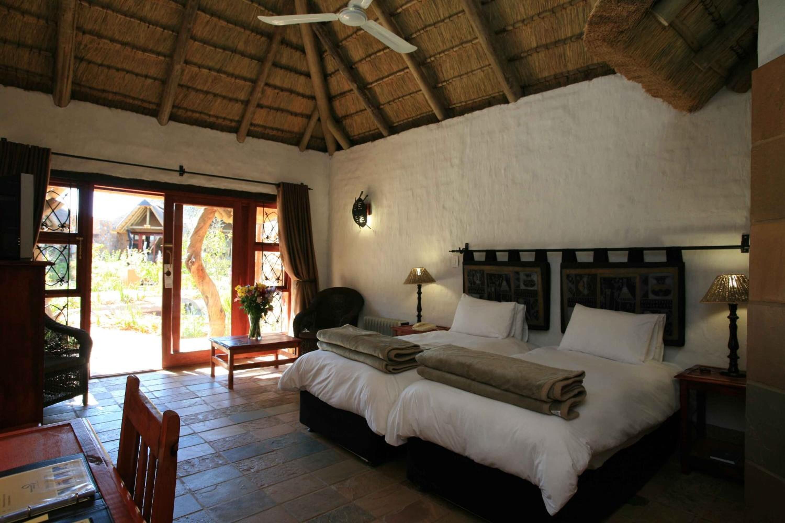 A bedroom with a large bed, a ceiling fan, and a view of the outdoors through a glass door.