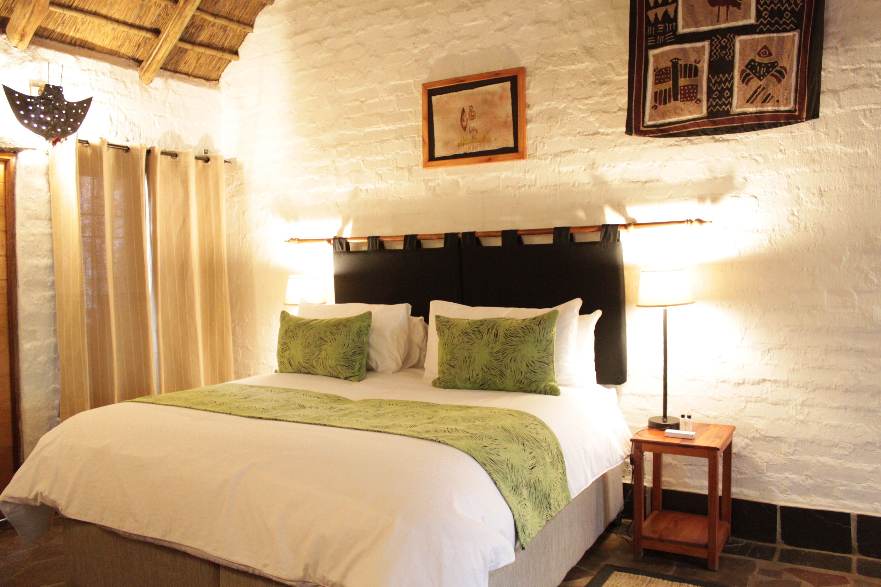 A neatly made bed with a green throw, a bedside lamp, and a framed picture on the wall.