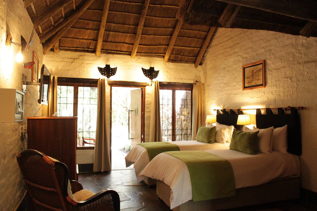 A room with two beds, a wooden chair, a desk, and a window with curtains.