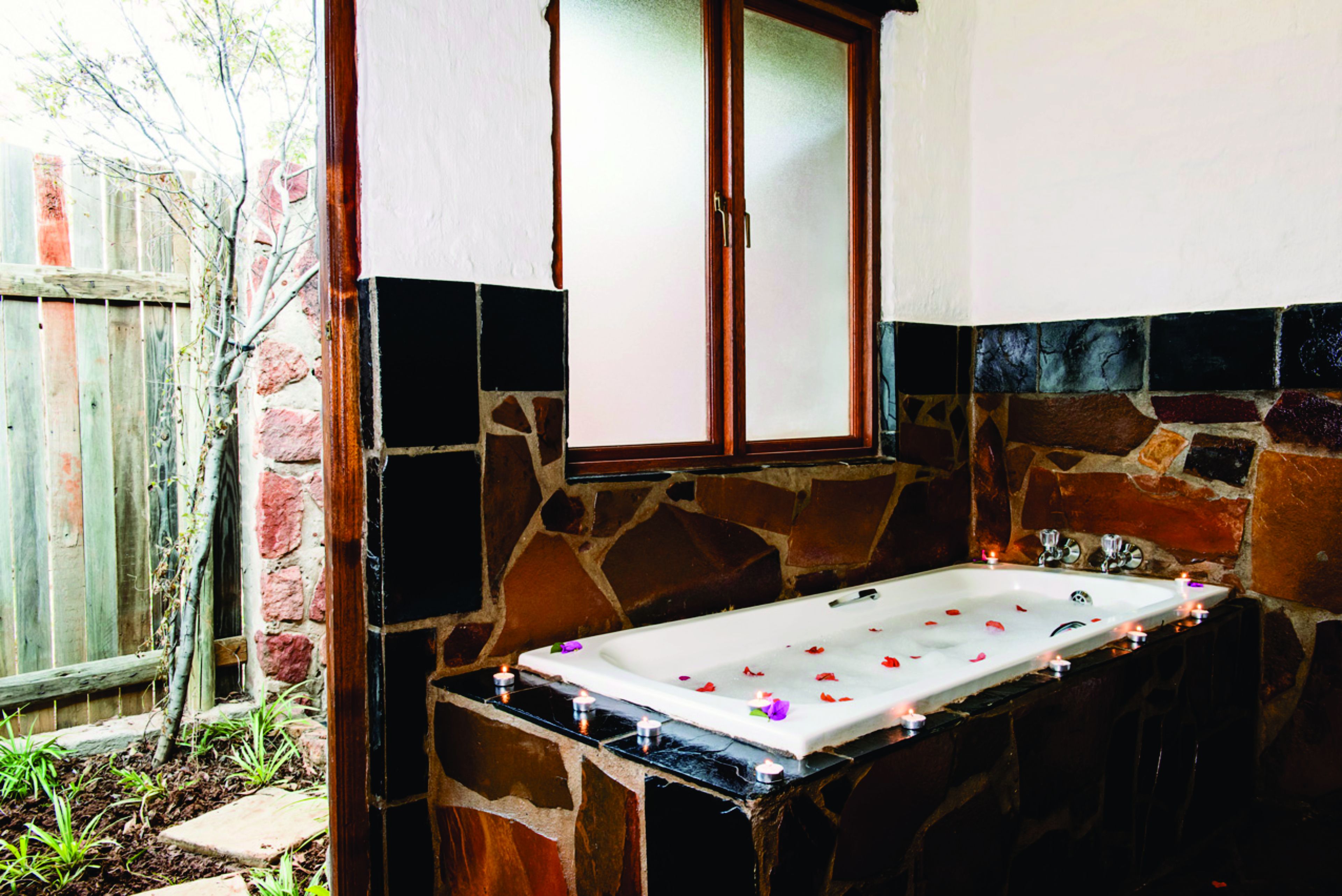 A stone-walled outdoor bathtub with a wooden window above it.
