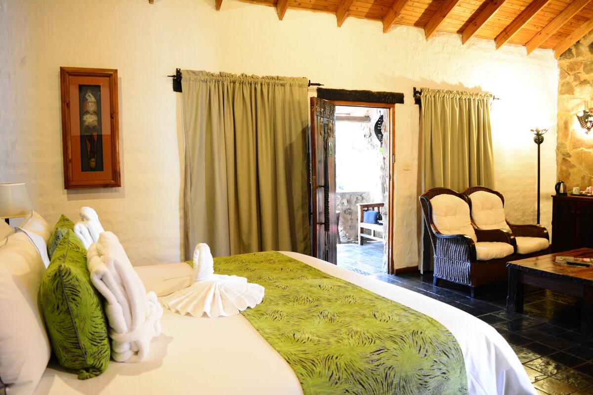 A hotel room with a bed, two chairs, a table, and a door leading to an outdoor area.