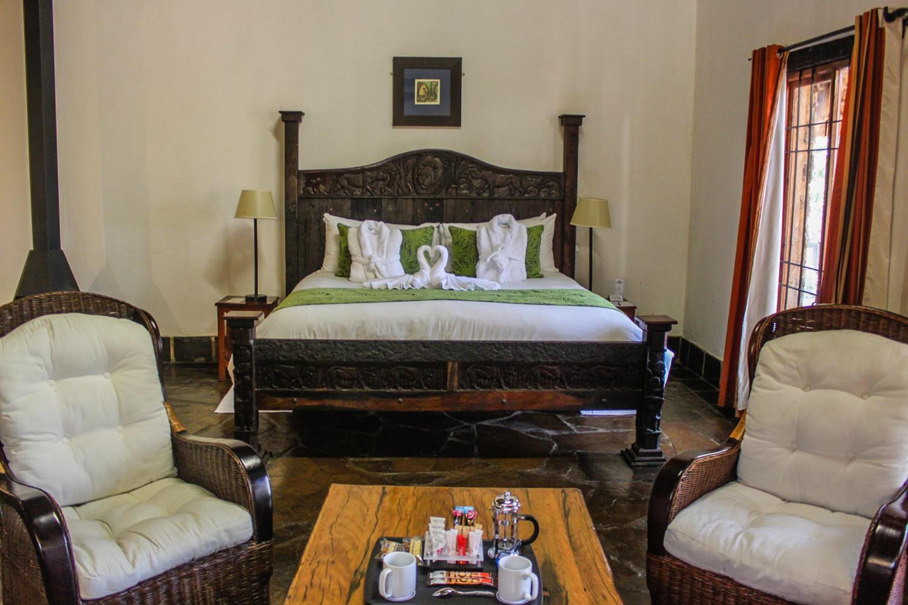 A hotel room with a large bed, two chairs, a coffee table with breakfast items, and a picture on the wall.