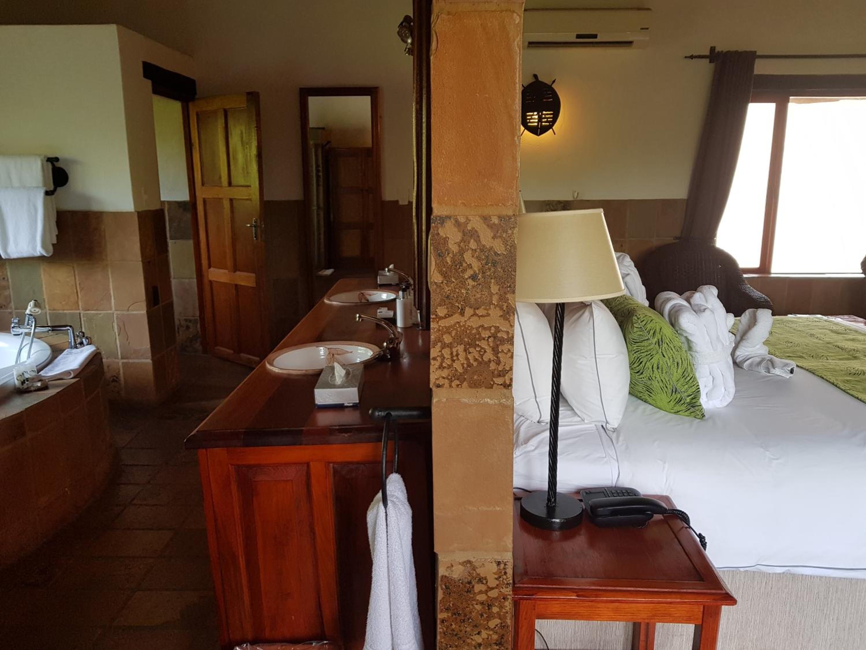 A hotel room with a wooden vanity, a bed with a green pillow, a lamp, and a telephone.