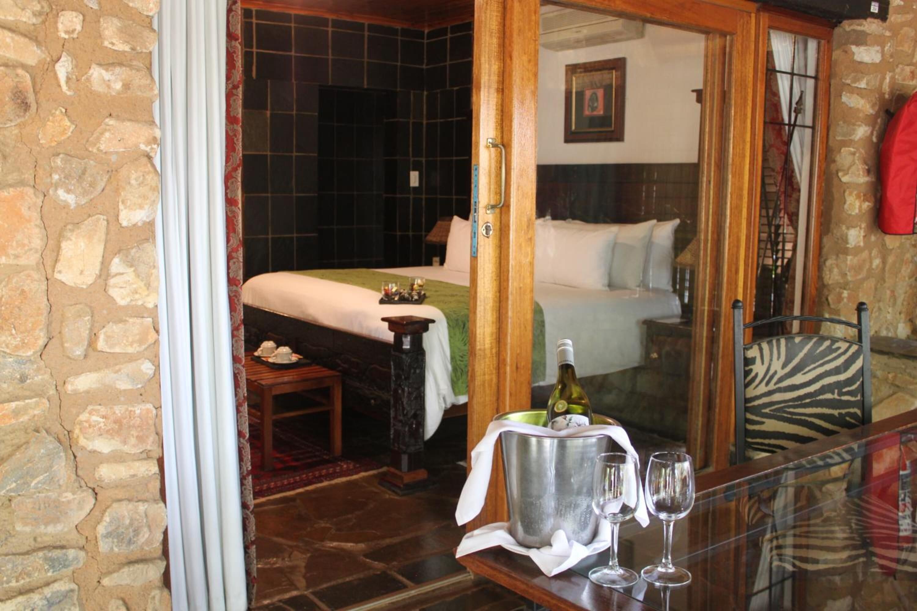 A room with a bed, a small table with a bottle and glasses, and a zebra-patterned chair.