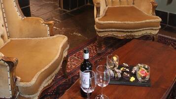 A room with two plush armchairs, a wooden table with a bottle and glasses, and a bed in the background.