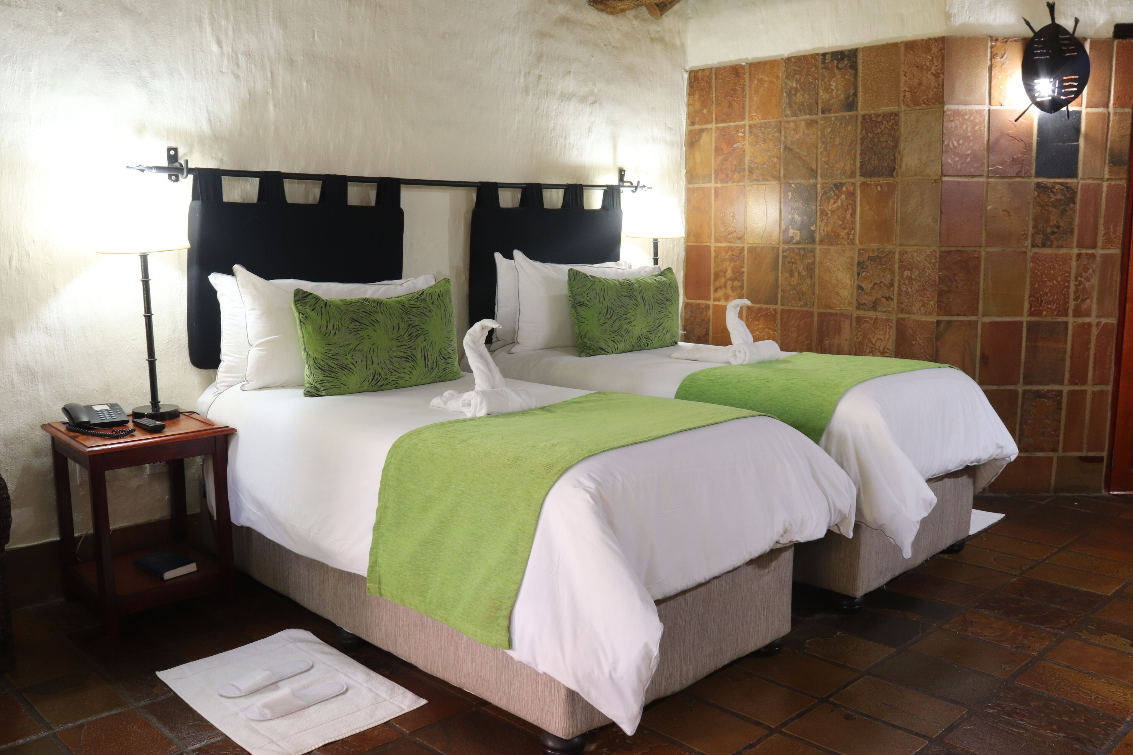 Una cama doble con una colcha verde y blanca, dos almohadas blancas y un cubreleche verde a juego.