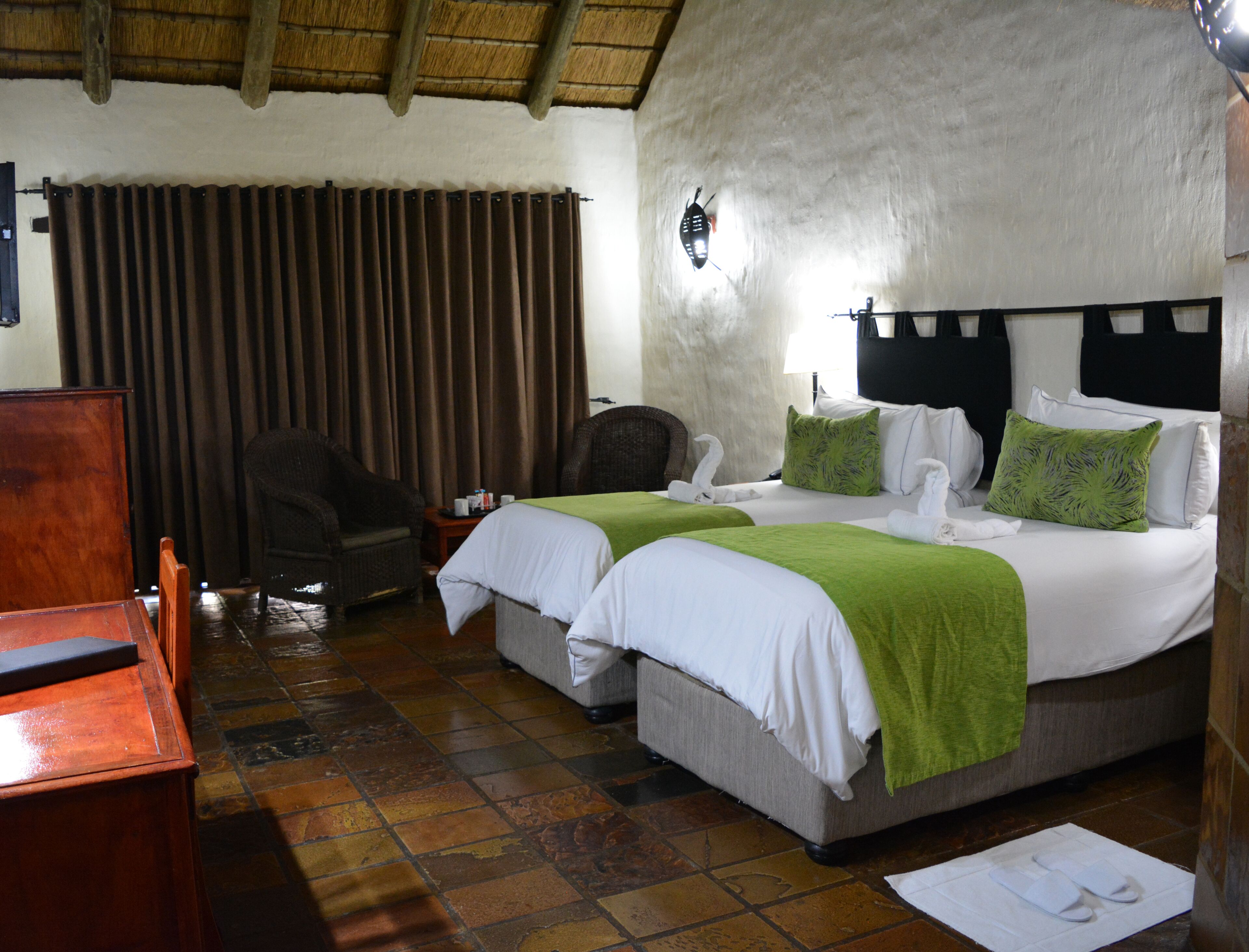 A hotel room with two beds, a wooden desk, a chair, a small table, and a curtain.