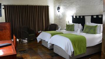 A hotel room with two beds, a wooden desk, a chair, a small table, and a curtain.