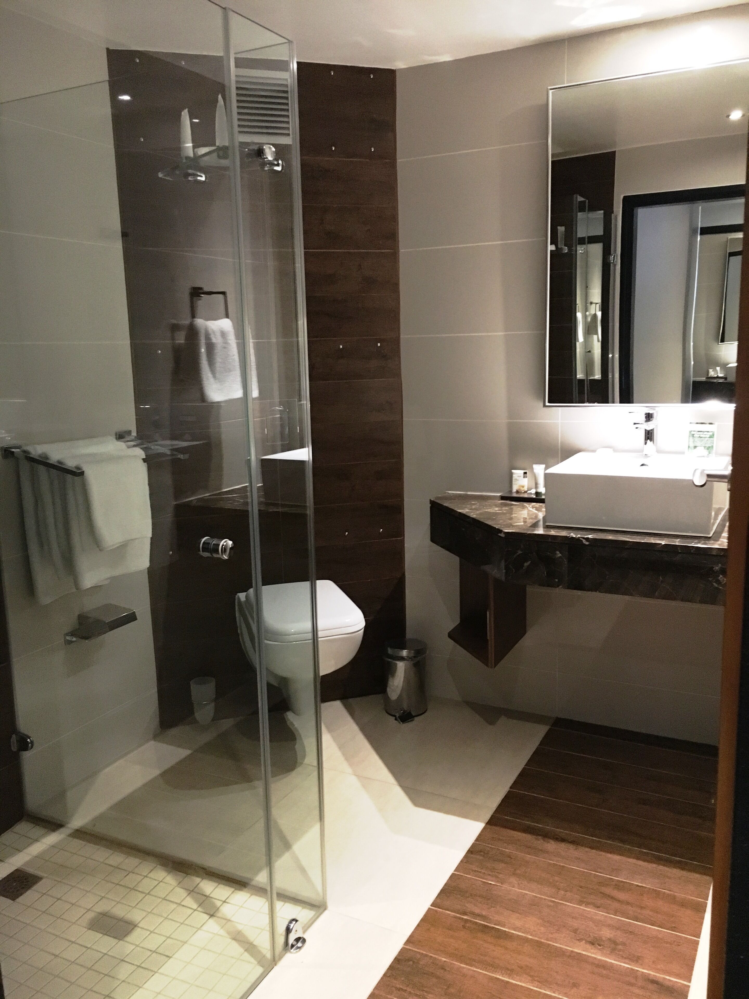 A modern bathroom with a glass shower enclosure, a white toilet, a sink with a mirror, and a tiled floor.