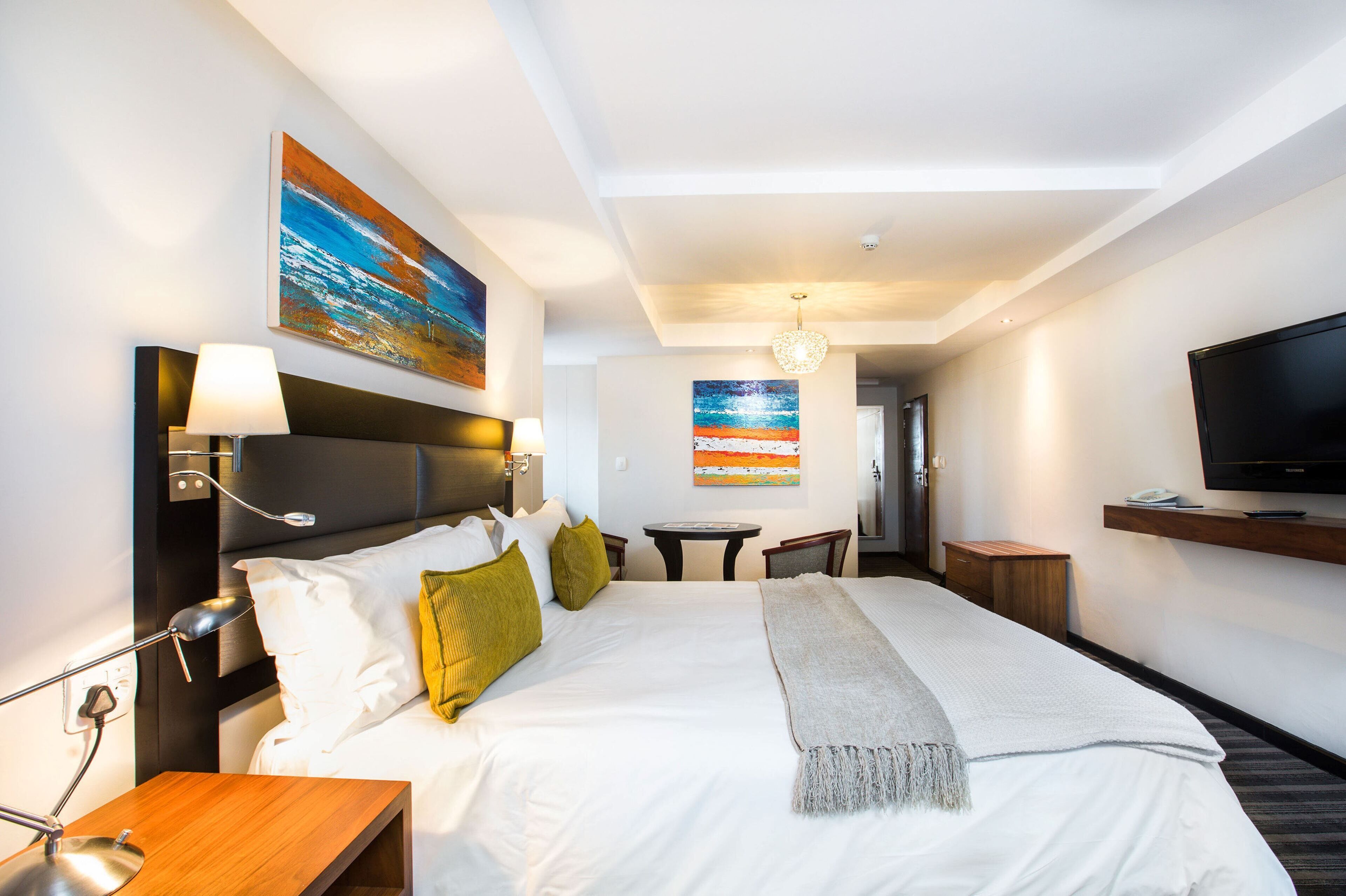A hotel room with a large bed, bedside tables, a TV, and artwork on the walls.