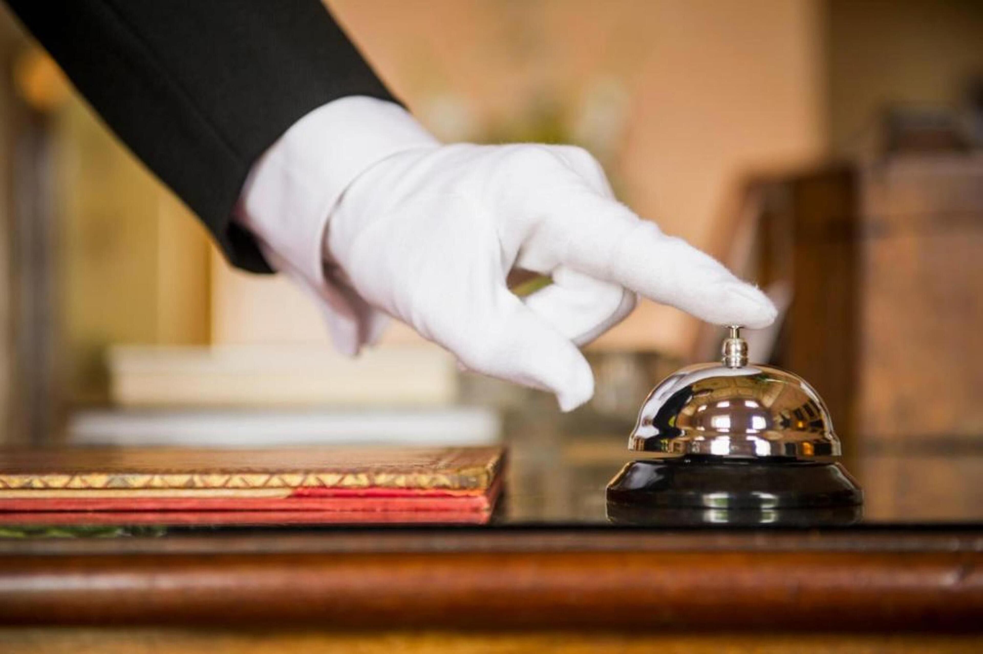 A hand in a white glove pressing a hotel room's bell.