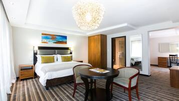 Habitación de hotel con cama, una mesa redonda con dos sillas, un armario de madera, un cuadro en la pared y una lámpara de araña.
