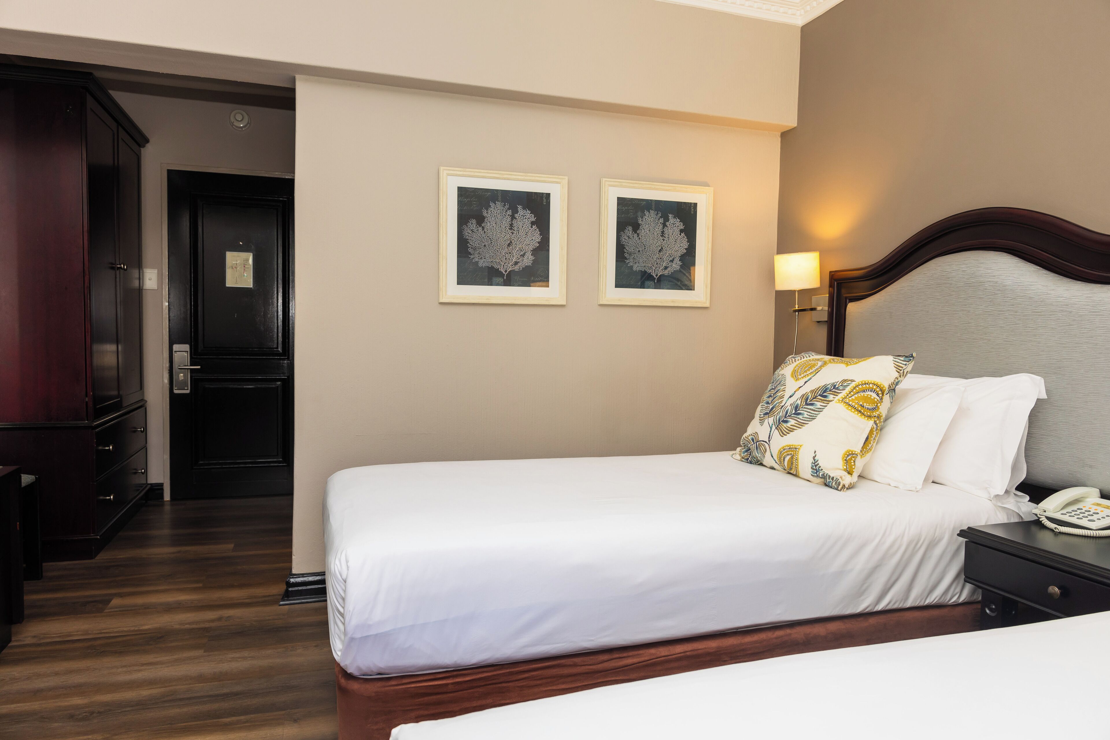 A hotel room with a double bed, a bedside table with a lamp, and two framed wall art pieces.