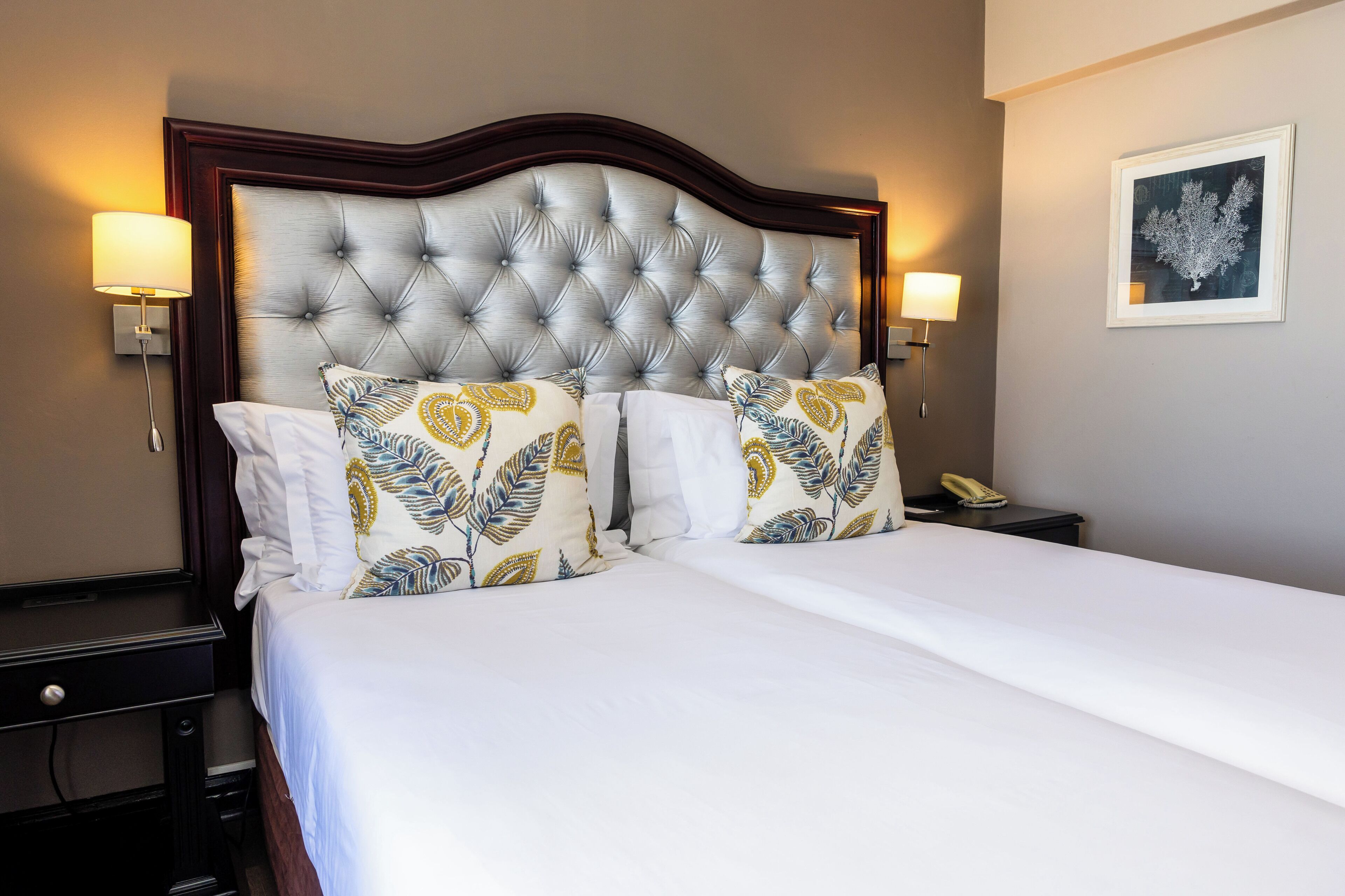 Una habitación de hotel con una cama grande, dos lámparas de noche, una mesita de noche y un cuadro en la pared.