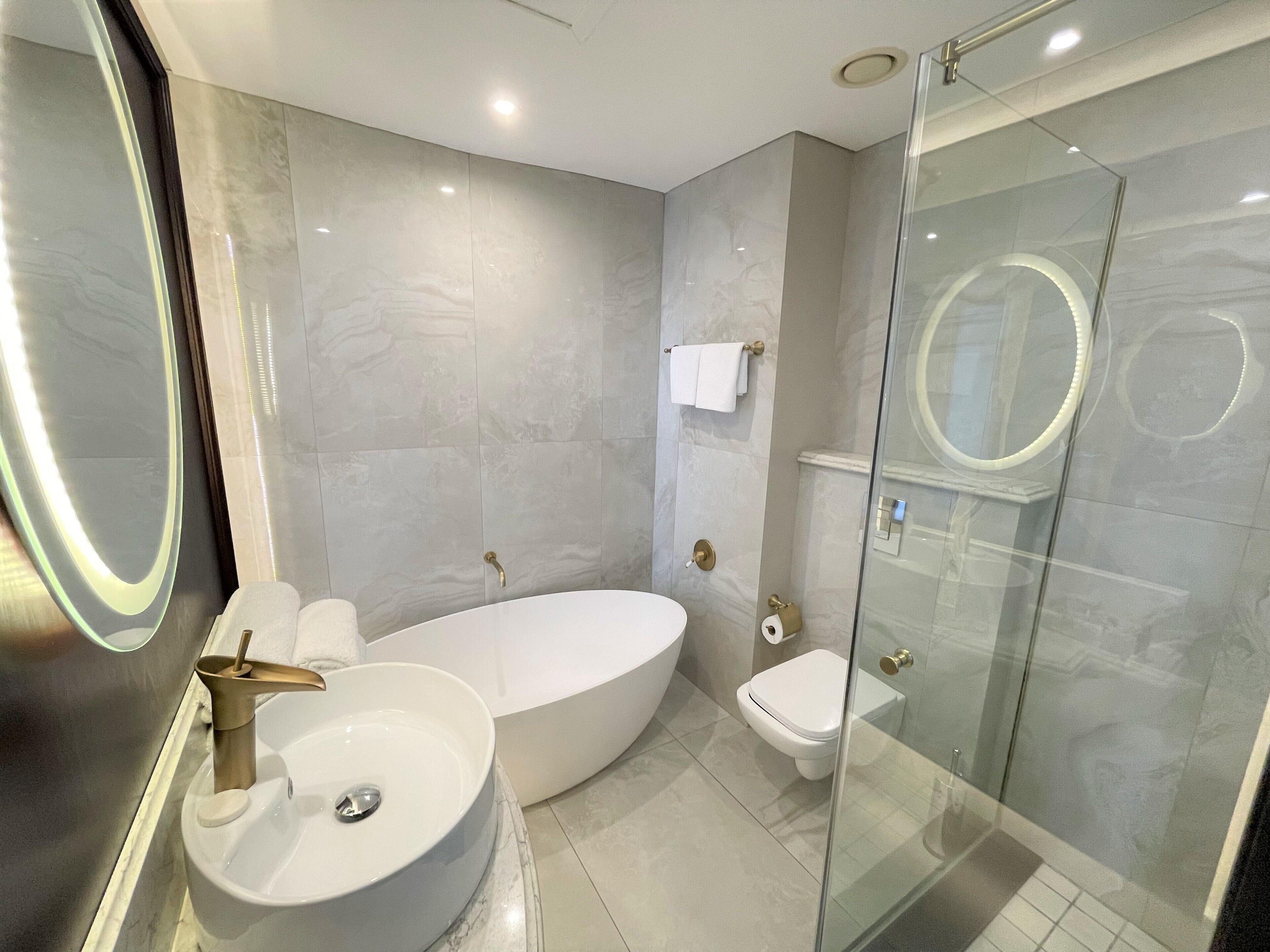 A modern bathroom with a large oval bathtub, a round sink, and a glass-enclosed shower area.