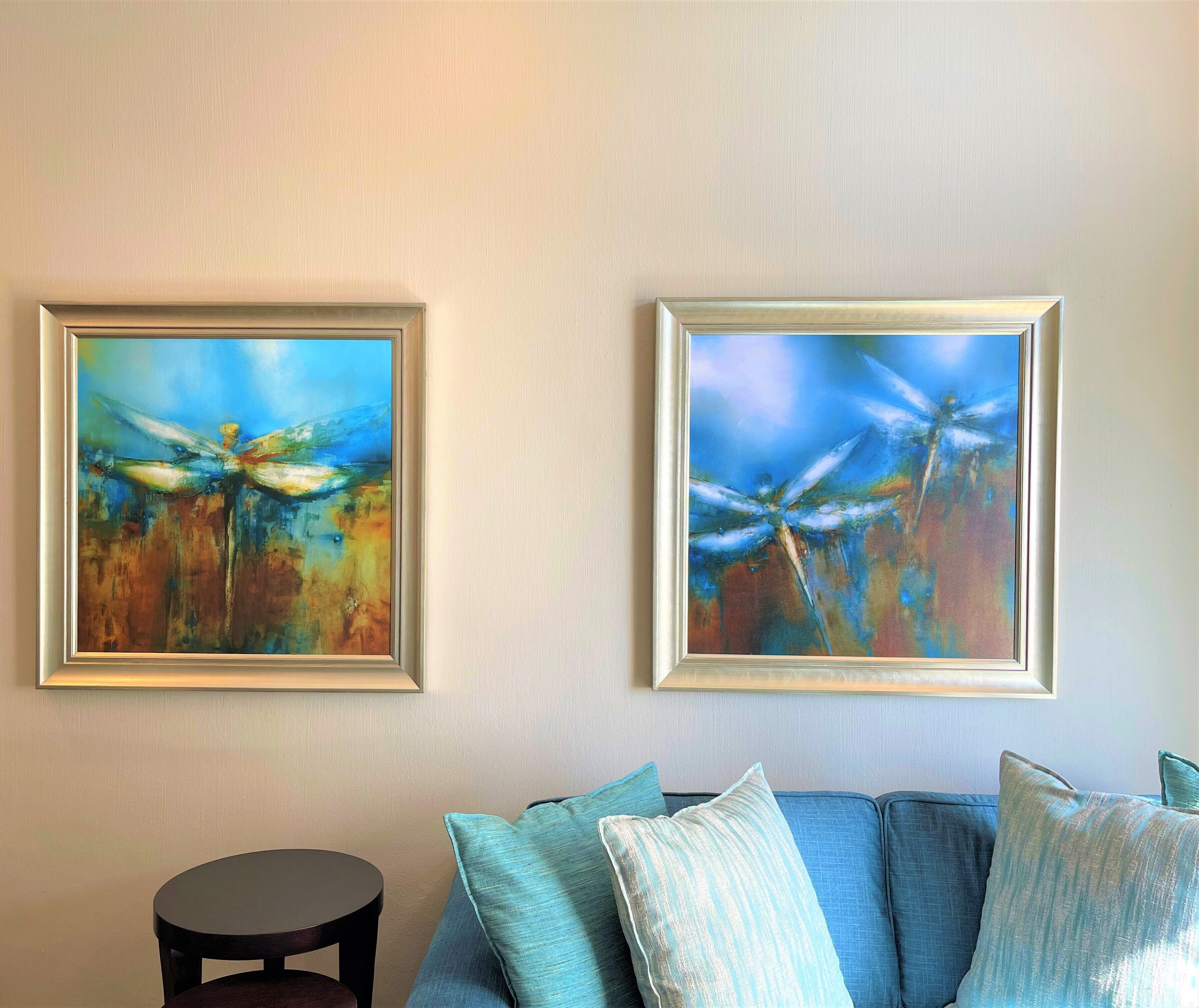 A room with two framed paintings of dragonflies on the wall, a blue sofa with matching cushions, and a small round table.