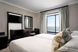 A hotel room with a large bed, a desk, a chair, a TV, and a window with curtains.