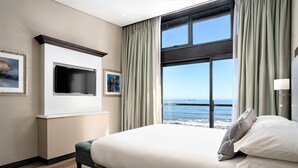 A hotel room with a large bed, a TV mounted on the wall, a view of the ocean, and a window with curtains. - Premier Hotel Cape Town (Cape Town)