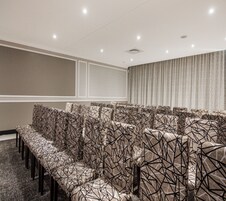 A conference room with rows of patterned chairs, a large screen on the wall, and a ceiling with recessed lighting.