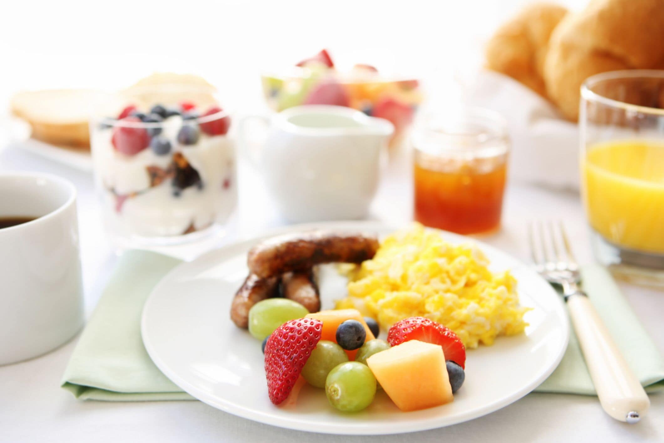 Prato de café da manhã com frutas, ovos mexidos e salsicha.