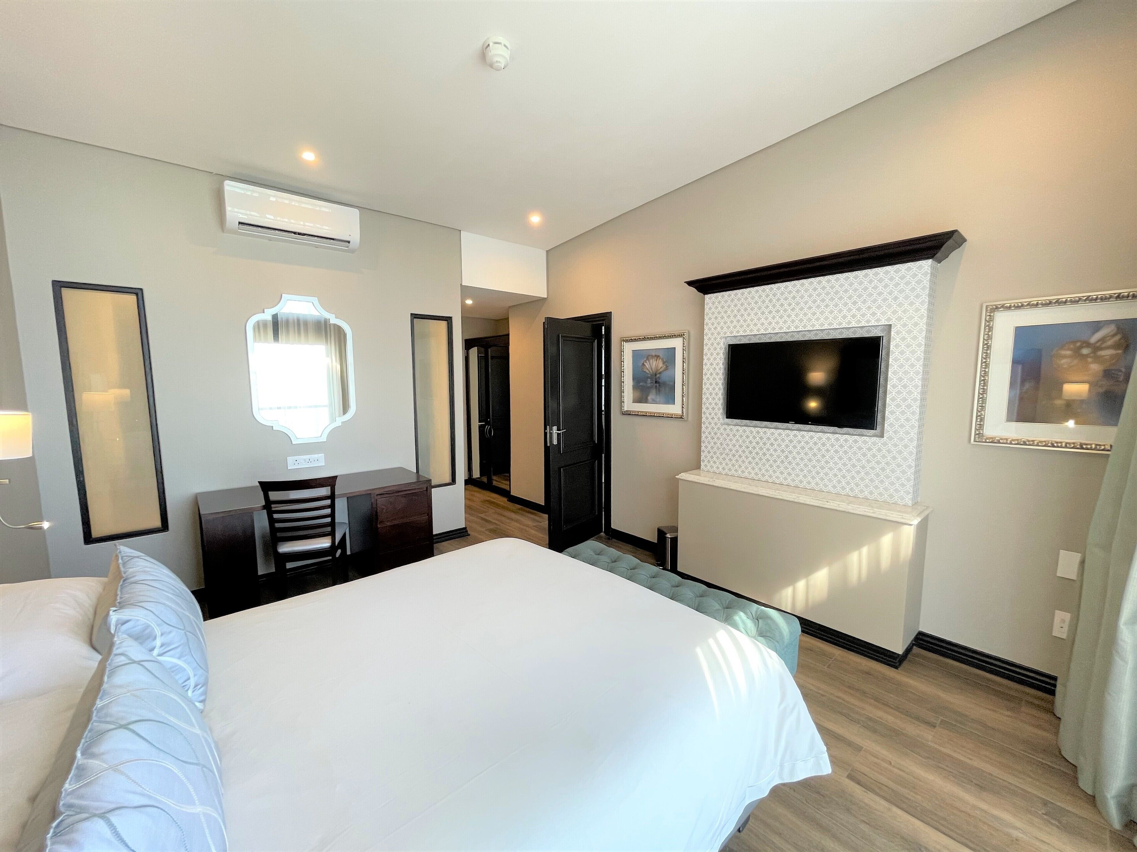A hotel room with a large bed, a desk, a chair, an air conditioning unit, a television, and framed artwork on the walls.