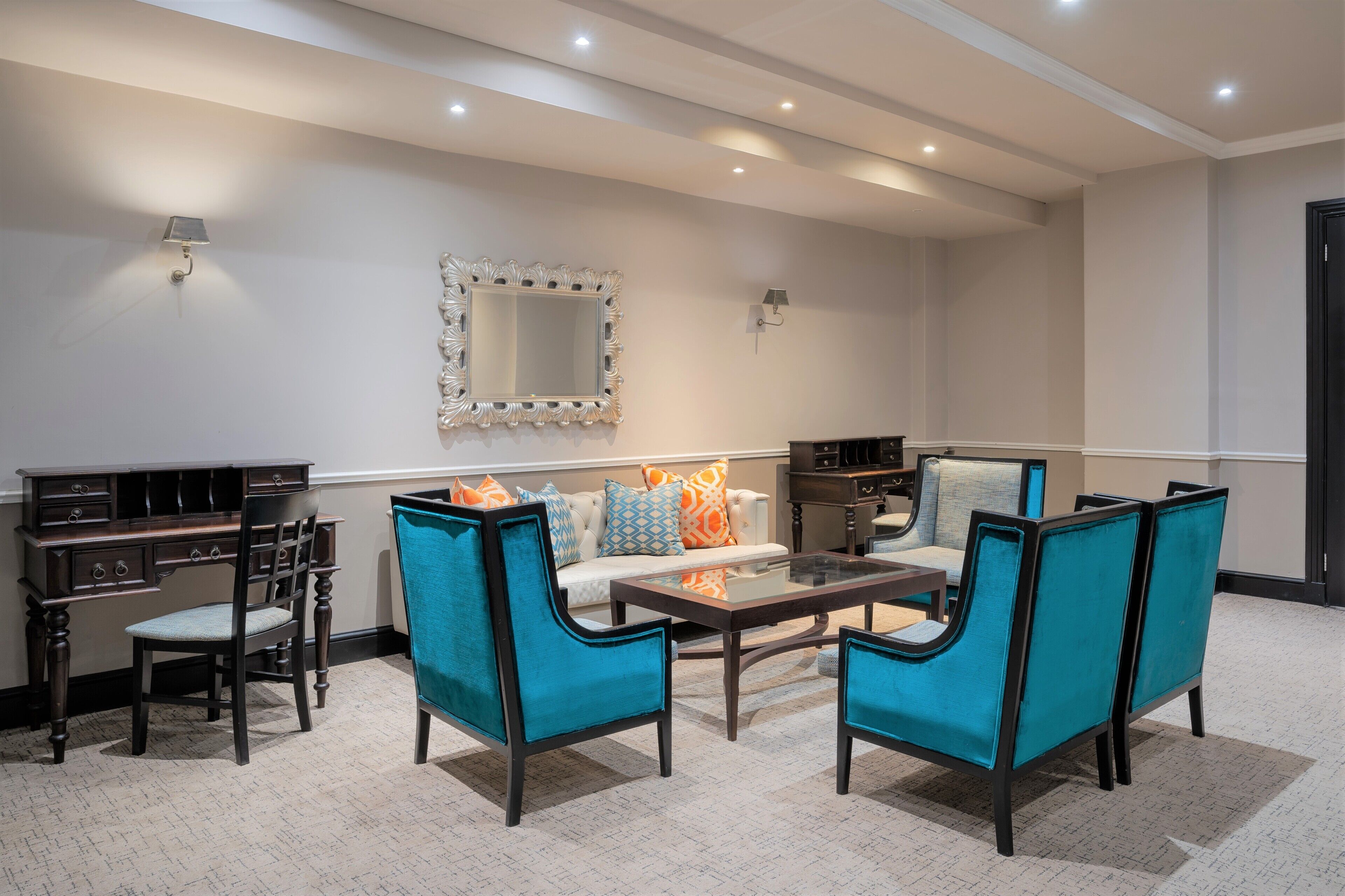 Una sala moderna con un sofá, dos sillones azules, una mesa de centro, un escritorio y un espejo.