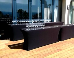 A table set with multiple wine glasses, a black tablecloth, and a view of palm trees through large windows.