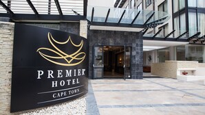The exterior of the Premier Hotel in Cape Town, featuring a prominent black sign with gold lettering, a modern architectural design with glass railings, and a stone-tiled entrance area. - Premier Hotel Cape Town (Cape Town)