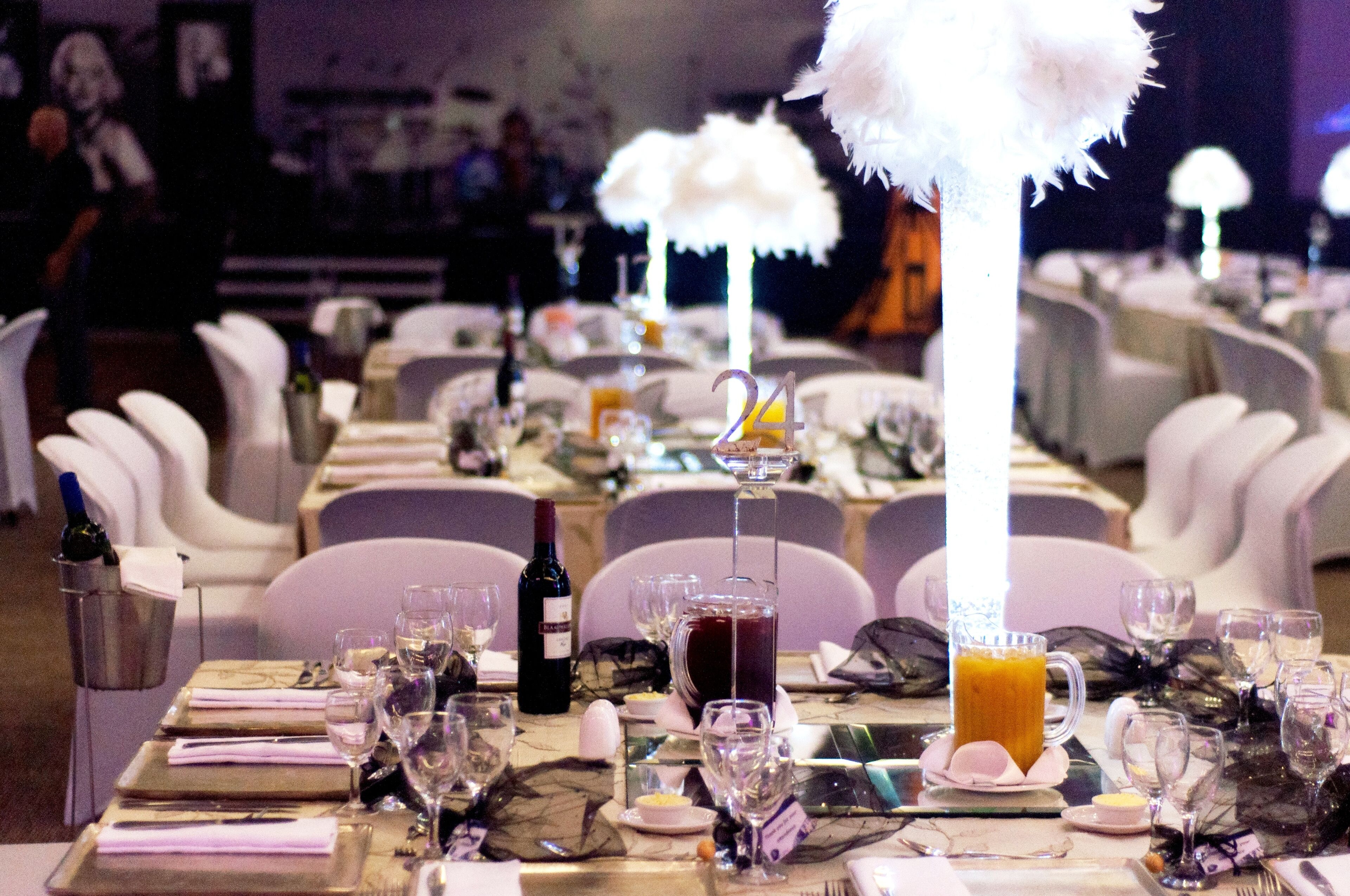 A banquet hall with round tables set for a formal event, featuring white chairs, table settings with wine glasses, and a central floral arrangement.
