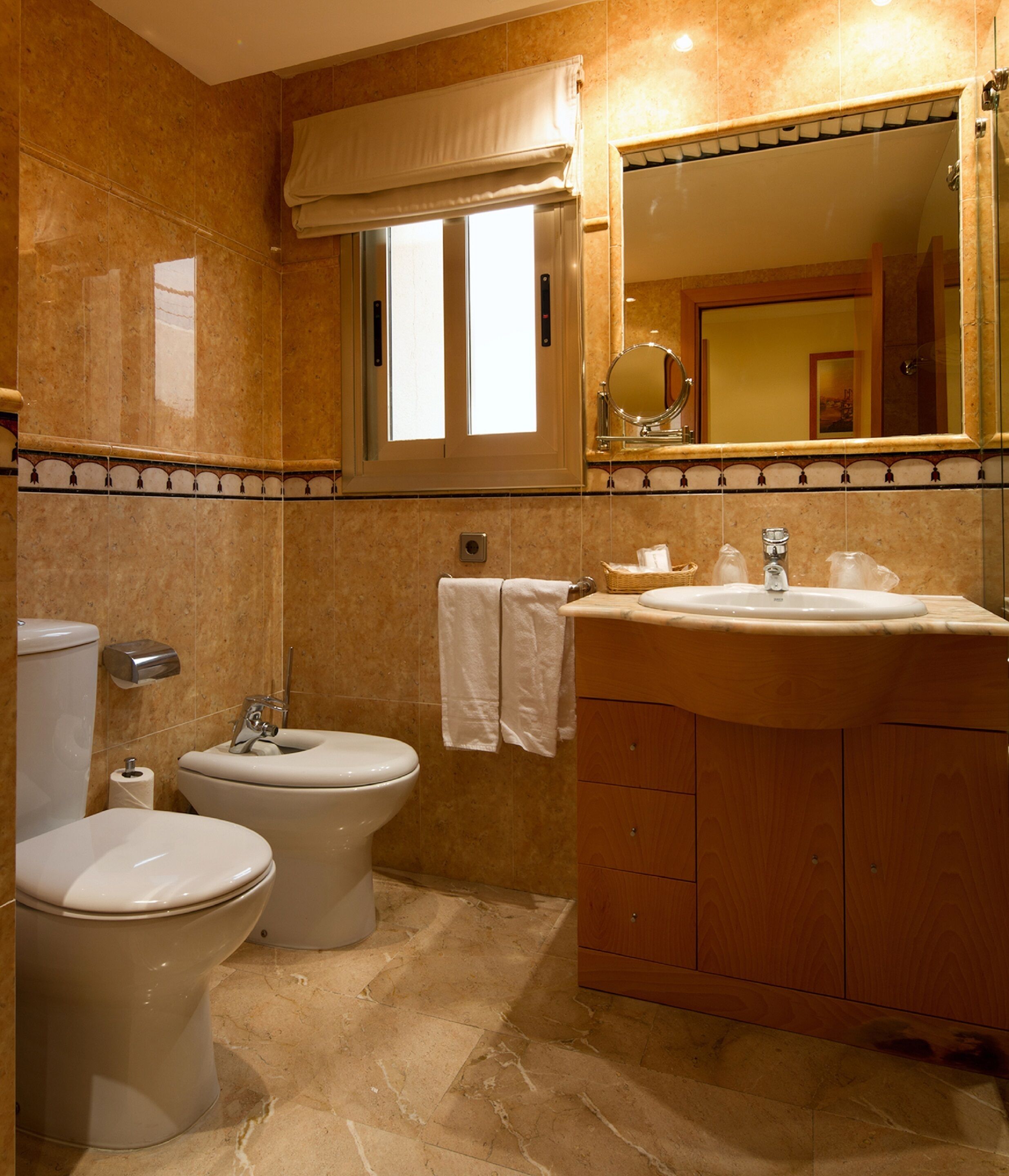 A bathroom with two toilets, a bidet, a sink, and a mirror.