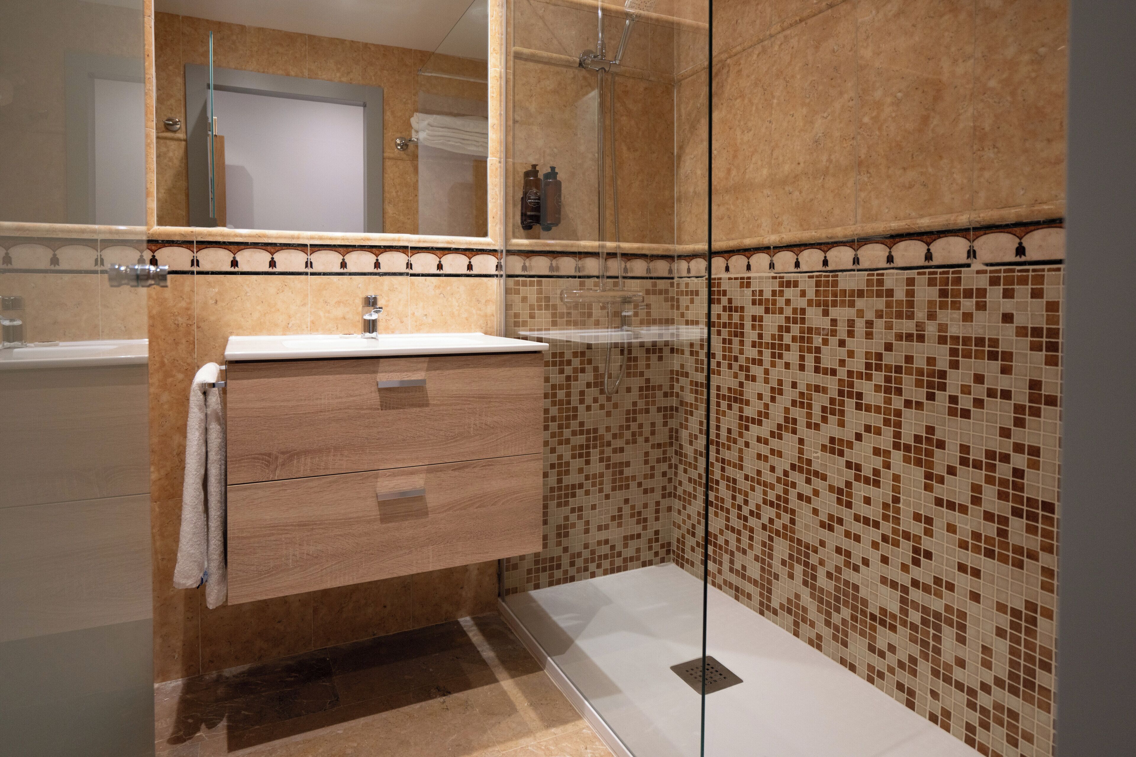 A bathroom with a glass-enclosed shower, a wooden vanity with a mirror, and tiled walls.