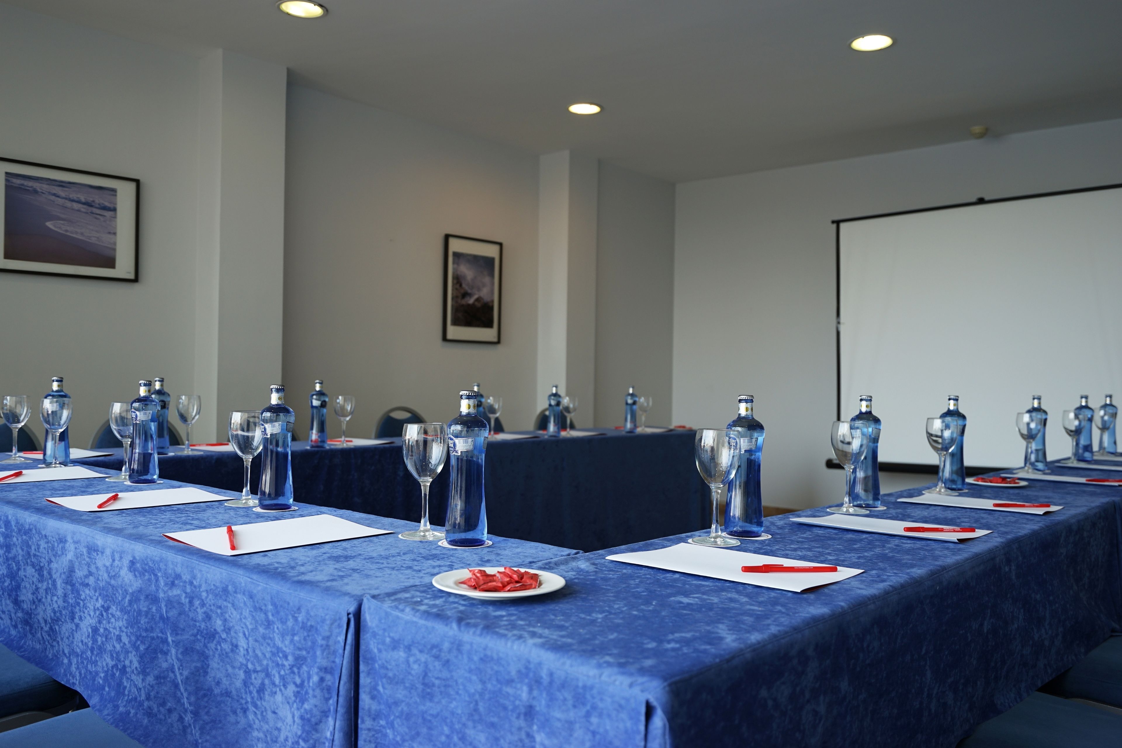 Ein Konferenzraum mit langem Tisch, vorbereitet für eine Besprechung, ausgestattet mit Wasserflaschen, Gläsern und Notizblöcken.