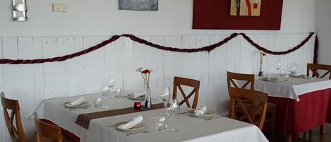 A dining area with tables set for a meal, chairs, and a decorative garland on the wall.