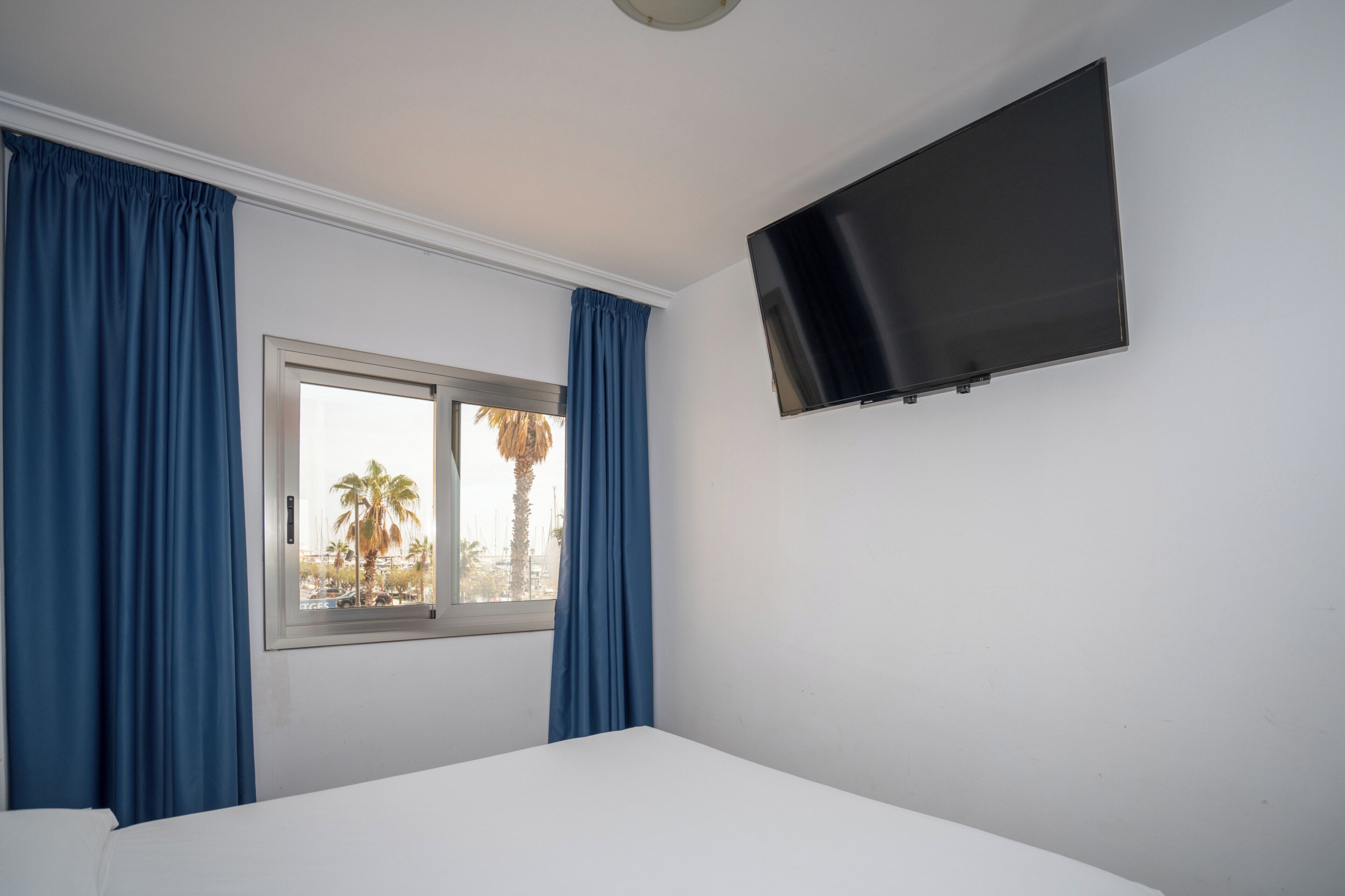 Una habitación con cama, ventana con cortinas y televisión montada.