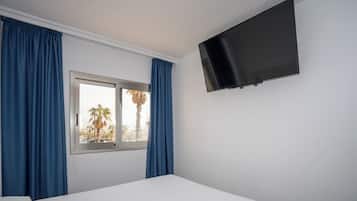 Una habitación con cama, ventana con cortinas y televisión montada.
